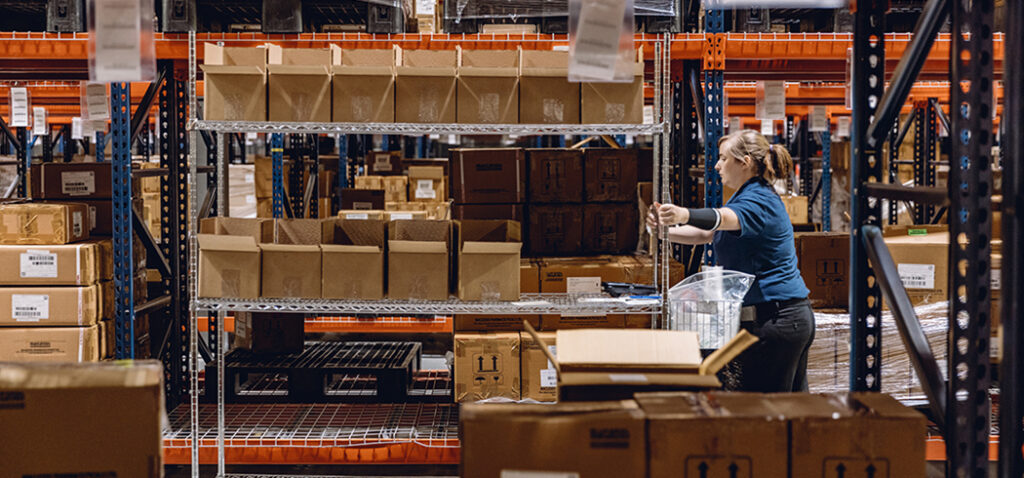 Worker Pushing Picking Cart with Boxes in MMI Warehouse